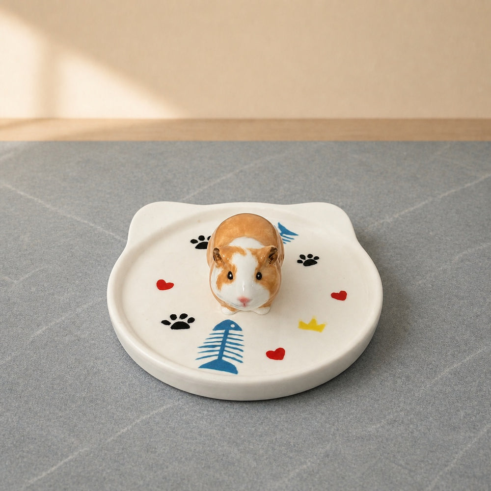 Tan and white guinea pig on a cat-face pet ring dish