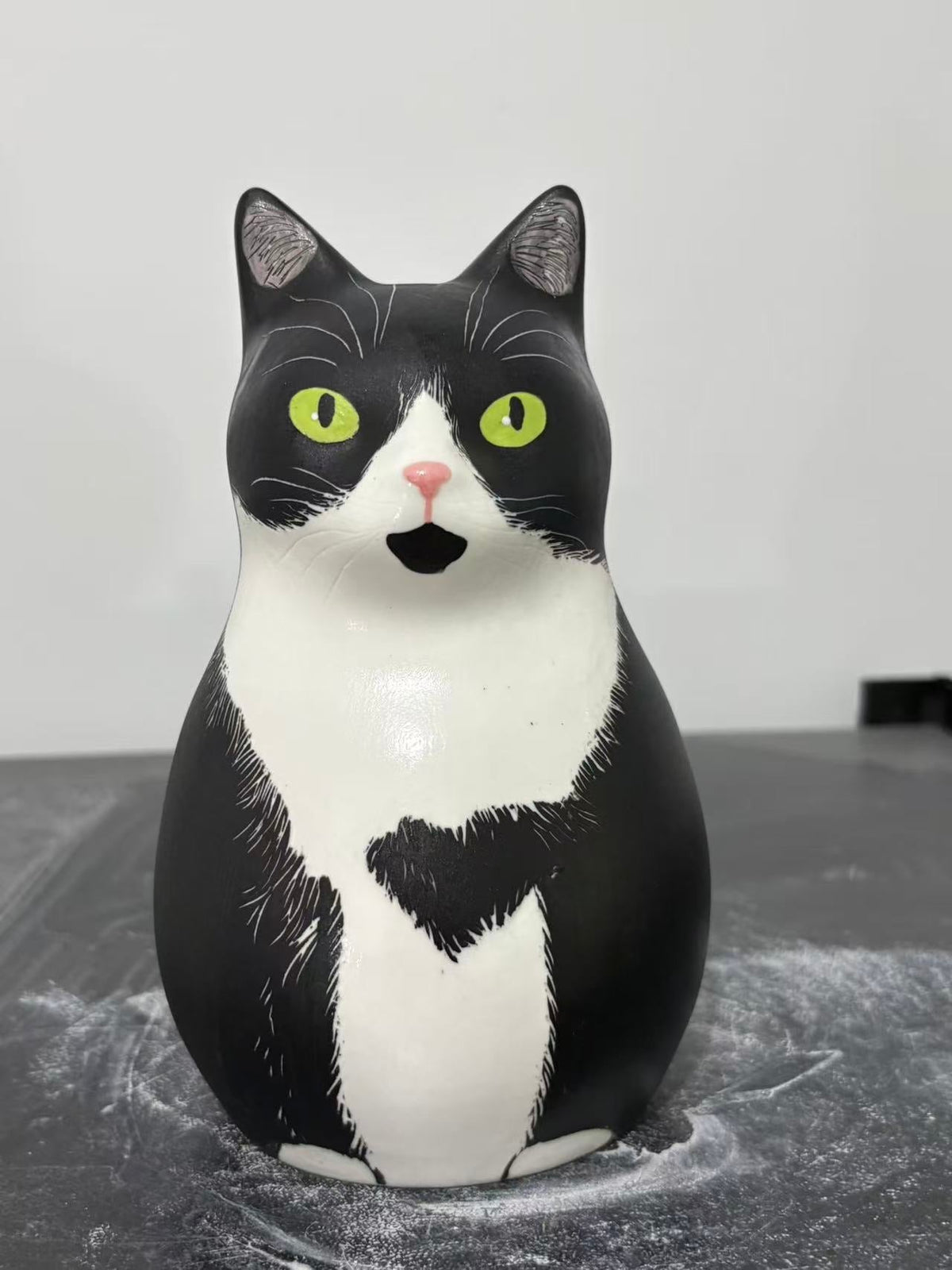 Front of a black and white cat urn with bright green eyes, pale muzzle, white chest and irregular dark marks along the lower body.