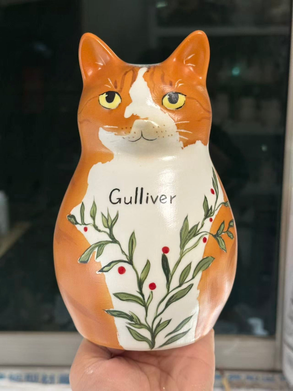 Ginger and white cat shaped ceramic held in a hand, with Gulliver lettering and a branching design.