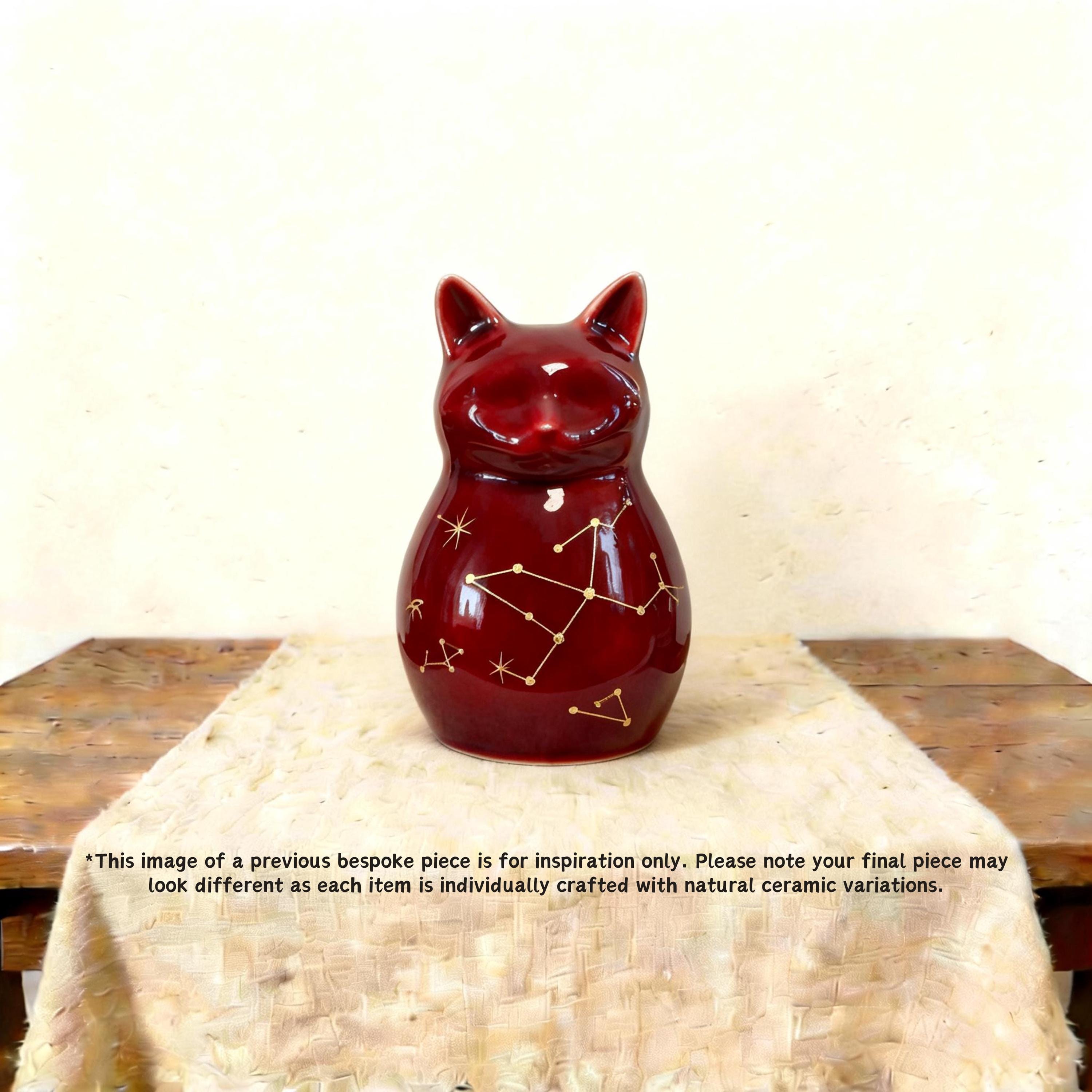 Styled on a shelf of a cat-shaped urn for human ashes — a handmade ceramic cat lover cremation urn, hand-painted and personalized, made to order from keepsake to full sizes by Farbe Ceramics.