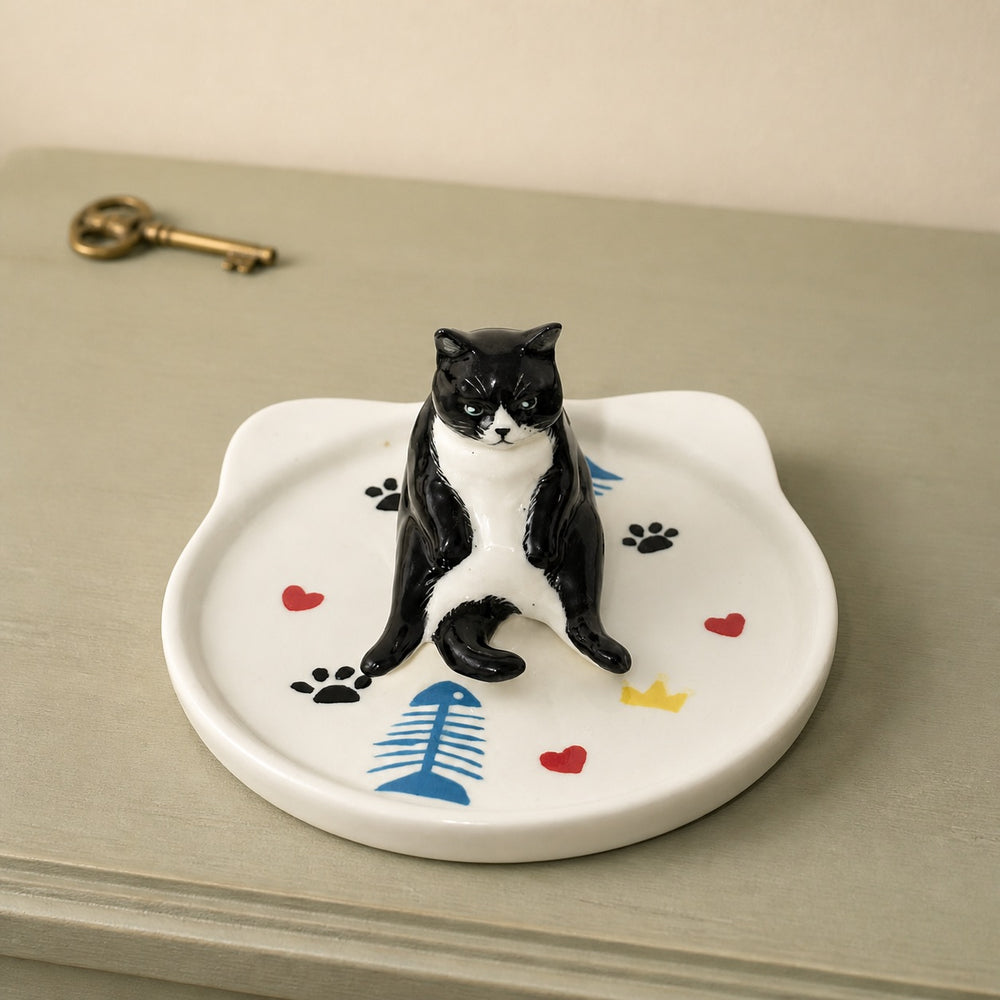Black and white tuxedo cat on a cat-face pet ring dish